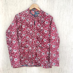 Puede incluir: Una chaqueta acolchada roja con estampado floral y dos bolsillos. La chaqueta tiene un cuello mandarín y cierre de botón.