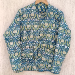 Puede incluir: Una chaqueta acolchada azul turquesa con estampado floral con flores blancas y verdes. La chaqueta tiene un cuello mandarín y cierre de botones.