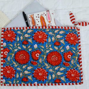 May include: A rectangular quilted fabric sleeve featuring a vibrant blue background with a repeating pattern of large red flowers and green leaves. The sleeve is edged with a red and white striped border and includes a matching red and white striped tie.