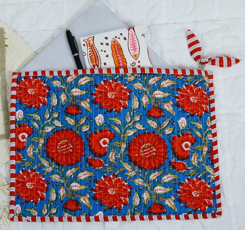May include: A rectangular quilted fabric sleeve featuring a vibrant blue background with a repeating pattern of large red flowers and green leaves. The sleeve is edged with a red and white striped border and includes a matching red and white striped tie.
