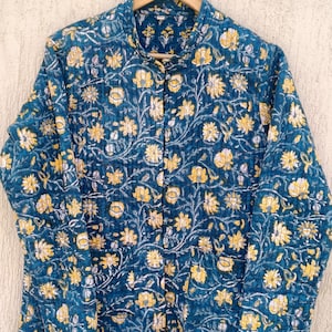 May include: A blue quilted jacket with a floral print in yellow and white. The jacket has a mandarin collar and a button closure.