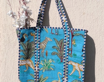 Può includere: Una borsa tote blu con un bordo a righe bianche e nere. La borsa presenta una stampa colorata di animali e piante, tra cui zebre, leopardi, tucani e palme.