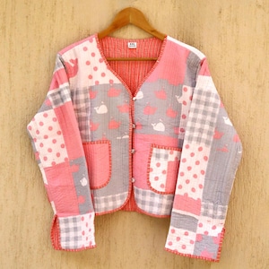 May include: A pink and grey quilted jacket with a button fastening and two patch pockets. The jacket has a patchwork design with different patterns, including polka dots, plaid, and whales. The label on the jacket says "XXL".