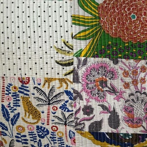 May include: A quilted textile featuring a patchwork design with distinct sections. One section has black polka dots on white, another shows a large orange flower, and others display a leopard, palm trees, and intricate pink floral patterns.