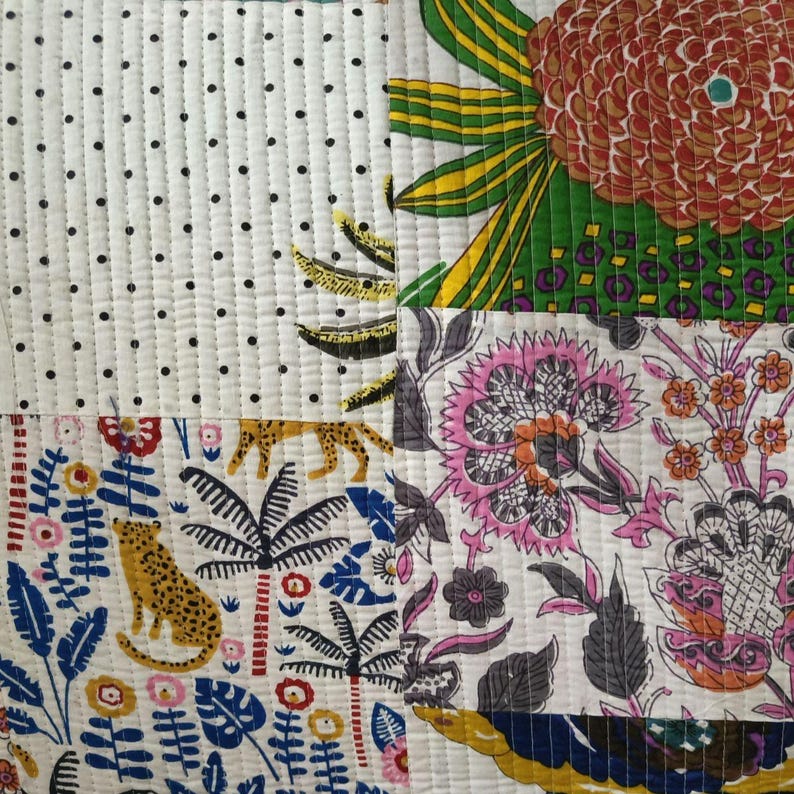 May include: A quilted textile featuring a patchwork design with distinct sections. One section has black polka dots on white, another shows a large orange flower, and others display a leopard, palm trees, and intricate pink floral patterns.