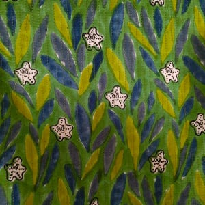 May include: A quilted fabric featuring a repeating pattern of white starfish with black outlines and facial features, set against a background of overlapping green and blue leaf-like shapes, with vertical stitching lines running across the textile.