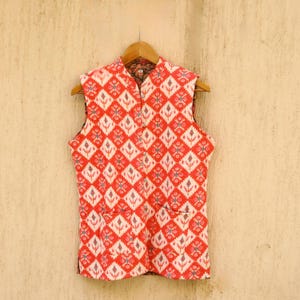 May include: A sleeveless red and white patterned waistcoat with a mandarin collar and two pockets.