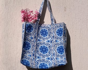 Può includere: Una borsa tote blu e bianca con un motivo floreale. La borsa ha un manico bianco ed è realizzata in tessuto intrecciato.