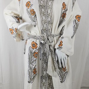 May include: White waffle weave robe with a floral print in shades of orange, gray, and black. The robe has a tie belt and a shawl collar.