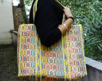 Op de afbeelding: Een grote tote bag met een kleurrijk bloemenpatroon. De tas heeft een herhalend ontwerp van bloemen in tinten geel, roze, blauw en groen. De tas heeft een rechthoekige vorm met een bijpassende band.