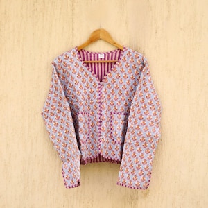 Puede incluir: Una chaqueta acolchada azul claro con estampado floral y forro a rayas rosa y blanco. La chaqueta tiene cierre de botón y dos bolsillos.