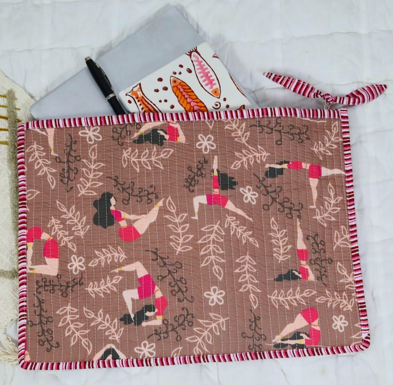 May include: A rectangular quilted fabric sleeve featuring a brown background with a repeating pattern of figures in yoga poses, white floral outlines, and leafy branches. The sleeve has a red and white striped fabric trim and a matching fabric tie.