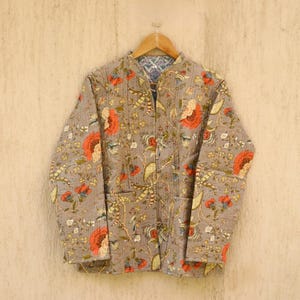 Könnte beinhalten: Eine graue gesteppte Jacke mit Blumenmuster. Die Jacke hat einen Reißverschluss und einen Stehkragen.