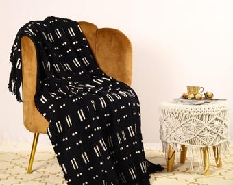 May include: Black and white patterned throw blanket with fringe, draped over a brown armchair. The blanket has a geometric design with white lines and dots on a black background.