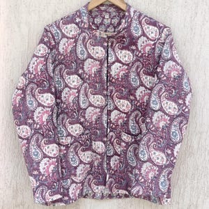 Könnte beinhalten: Eine lilafarbene gesteppte Jacke mit Paisley-Muster. Die Jacke hat einen Stehkragen und einen Knopfverschluss.