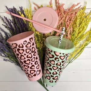 May include: Two reusable tumblers with lids and straws. The tumblers are pink and green with a brown leopard print design. The lids are solid pink and green.