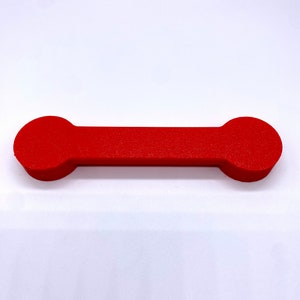 May include: A red, cylindrical phone holder with rounded ends. The holder is made of a smooth, solid material.