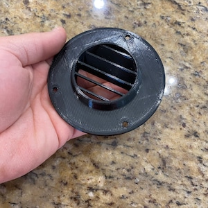 May include: Black plastic vent cover with a round shape and a rectangular grill design.