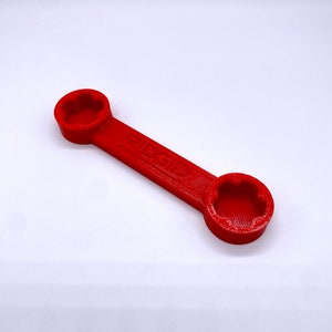 May include: A red plastic wrench with two hexagonal openings. The wrench has the word "GIBSON" printed on it.