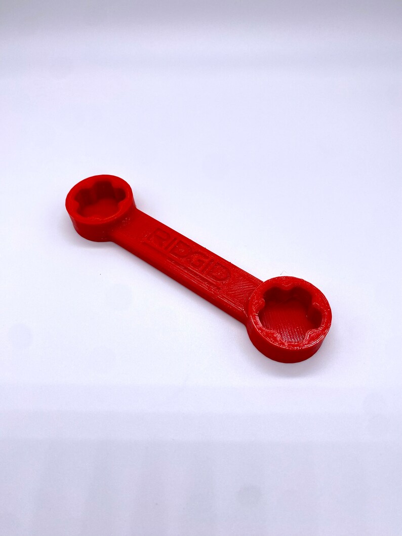 May include: A red plastic wrench with two hexagonal openings. The wrench has the word "GIBSON" printed on it.