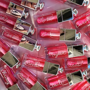 A group of pink lip glosses that have been engraved with first names in calligraphy script.