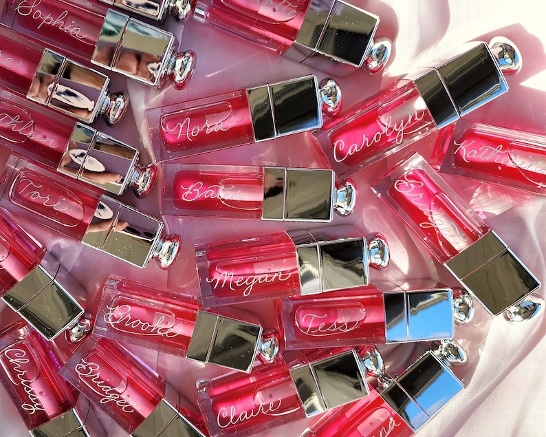 A group of pink lip glosses that have been engraved with first names in calligraphy script.