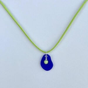 May include: A necklace with a blue sea glass pendant and a green glass bead. The necklace is made with a green suede cord.