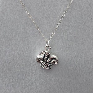May include: Silver necklace with a chef hat charm. The charm has the word "CHEF" inscribed on it.