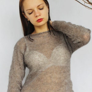 Può includere: Un maglione trasparente a maniche lunghe, marrone chiaro. Il maglione è abbinato a pantaloncini neri con bottoni dorati. Fiori secchi e rami sullo sfondo.