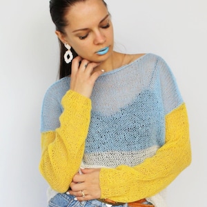 Puede incluir: Un suéter de bloques de color en azul, amarillo y blanco. La parte superior de punto de manga larga tiene un ajuste relajado y se usa con pantalones cortos de mezclilla. Las mangas son de color amarillo brillante y el cuerpo es una mezcla de azul y blanco.