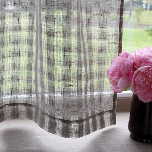 May include: A window with sheer, textured curtains and a black mug holding pink peonies. The curtains are a light gray with a woven pattern, and the flowers are a vibrant pink. The mug sits on a windowsill.