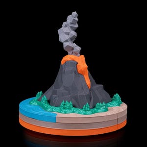 May include: A 3D printed low-poly volcano model featuring a dark gray mountain, bright orange lava flow, and a gray smoke plume. The base includes a blue river, green trees, and tan terrain, all set on a layered orange and tan circular platform.