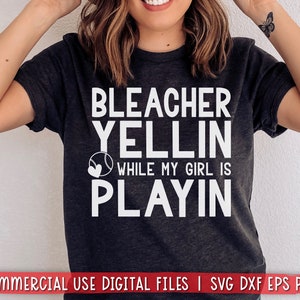 May include: A dark gray t-shirt with white text that reads "Bleacher Yellin While My Girl Is Playin" with a baseball and heart graphic.