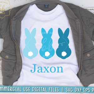 May include: A white t-shirt with three blue bunny silhouettes and the name Jaxon printed in blue. The bunnies have white tails and are arranged in a row.