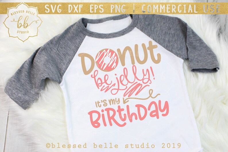 Op de afbeelding: Een wit T-shirt met een grijze mouw, met een roze en bruine donut-afbeelding met de tekst "Donut be jelly! It's my Birthday".
