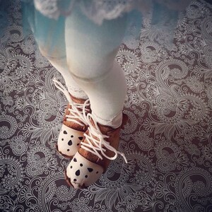 May include: A pair of brown leather shoes with white laces and white accents. The shoes have a decorative pattern on the toe and are worn by a person with white tights and a white and blue skirt.