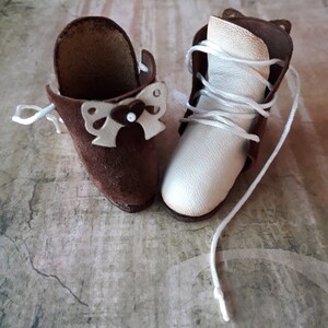 May include: A pair of miniature leather boots with laces. One boot is brown suede with a white bow detail, the other is white leather.