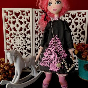 May include: A handmade doll with pink hair, wearing a black dress with pink floral embroidery, black shoes, and pink tights. The doll is holding a black purse with a gold chain and white flowers.