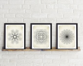 May include: Three black framed prints with white mats and a cream background. Each print features a different geometric design in black lines.