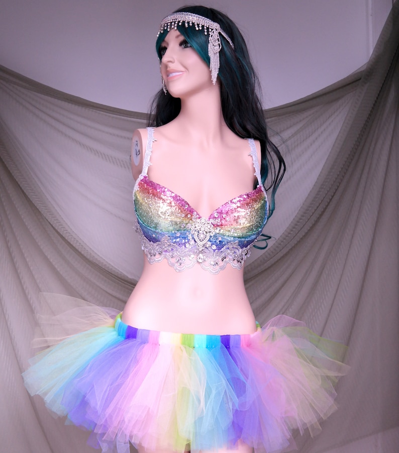 May include: A rainbow sequined bra with a silver lace trim and a rainbow tulle skirt. The skirt has a rainbow stripe waistband.