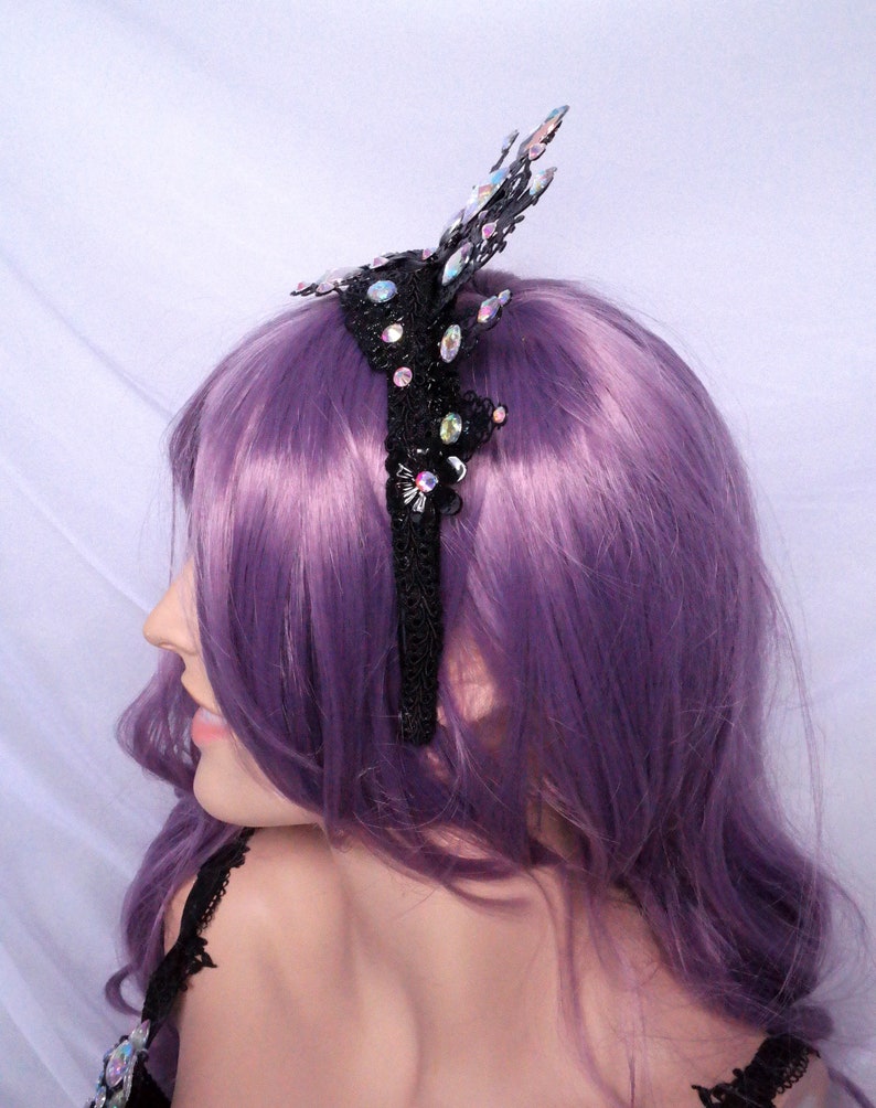 May include: A black lace headband with iridescent rhinestones and a butterfly design. The headband is worn on a model with purple hair.