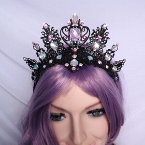 May include: A black metal crown with an intricate design and iridescent pink and clear gemstones.