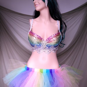 May include: A rainbow sequined bra with a silver lace trim and a rainbow tulle skirt. The bra has a rhinestone embellishment in the center.