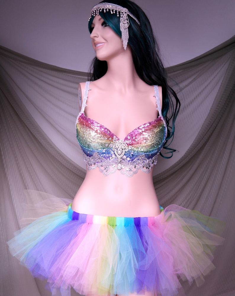 May include: A rainbow sequined bra with a silver lace trim and a rainbow tulle skirt. The bra has a rhinestone embellishment in the center.