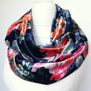 Puede incluir: Una bufanda infinita de terciopelo azul marino con estampado floral en tonos rosa, rojo y blanco.