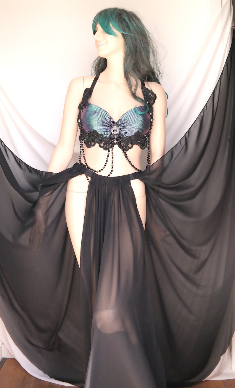 May include: A black sheer skirt with a high slit and a beaded belt. The skirt is paired with a black and iridescent bra top with lace trim.