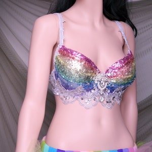 May include: A rainbow sequined bra with a silver lace trim and a large rhinestone embellishment in the center. The bra is worn over a rainbow tulle skirt.