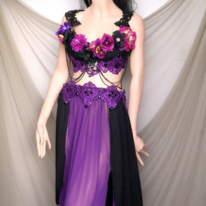 May include: A black and purple costume with floral accents and a jeweled crown. The top is black with purple flowers and lace detailing. The skirt is purple with black side panels. The costume is displayed on a mannequin.