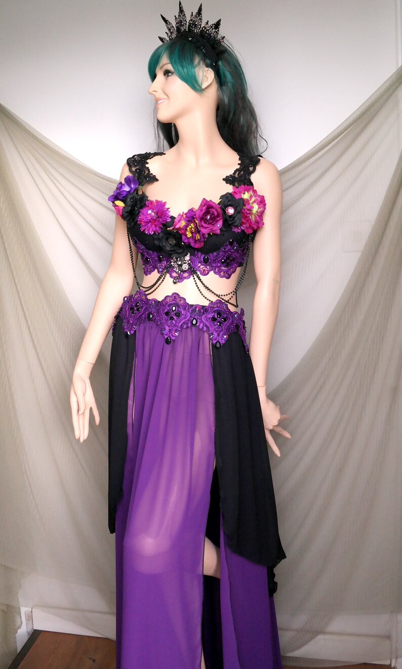 May include: A black and purple costume with floral accents and a jeweled crown. The top is black with purple flowers and lace detailing. The skirt is purple with black side panels. The costume is displayed on a mannequin.