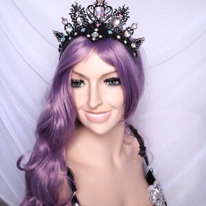 May include: A black wire crown with iridescent rhinestones and black beads. The crown is worn by a person with purple hair.